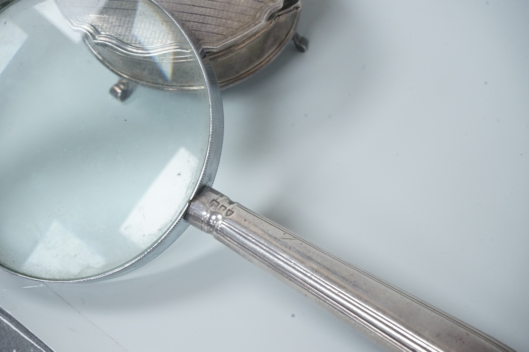 A George V silver mounted trinket box, by Adie Brothers, Birmingham, 1924, diameter 89mm. and a chrome magnifying glass, later added to a knife handle, handle by Goldsmiths & Silversmiths Co Ltd, London, 1894, 21.7cm.